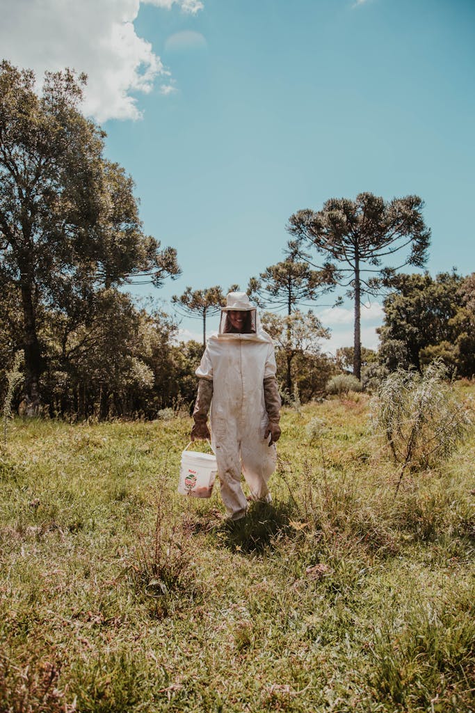 A beekeeper in protective gear walking through a lush green field on a sunny day.